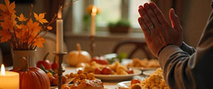 A card with a background of thanksgiving dinner table with food, hands clasped in prayer, and a festive greeting message.